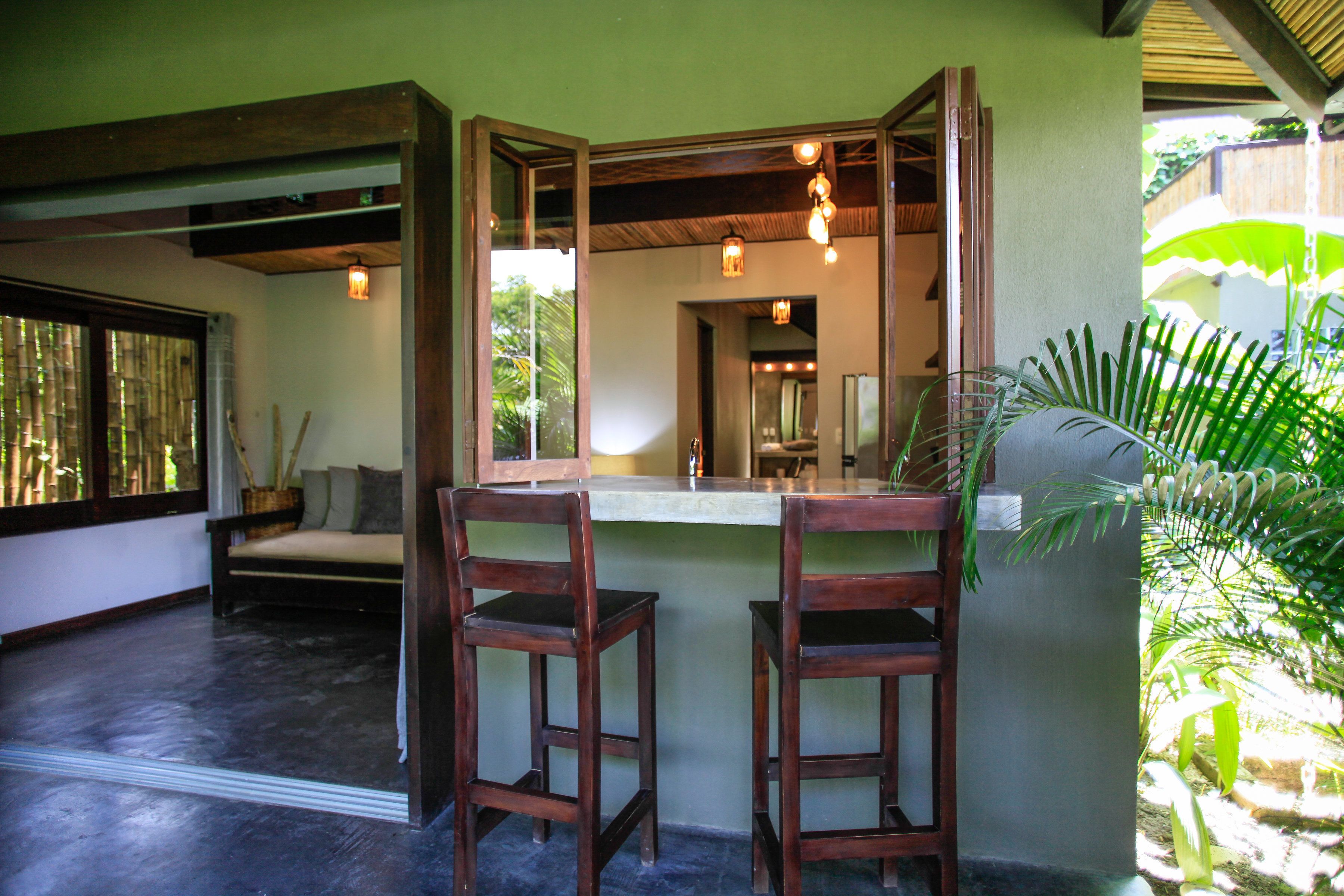 A room with a wooden bench, two wooden chairs, a mirror, and a window with bamboo blinds.
