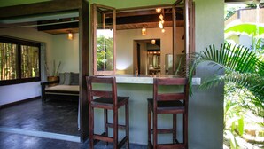 A room with a wooden bench, two wooden chairs, a mirror, and a window with bamboo blinds. - Lua Villas (Cóbano)