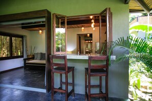 A room with a wooden bench, two wooden chairs, a mirror, and a window with bamboo blinds.