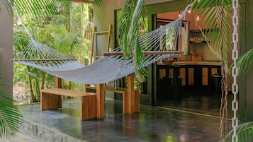 A hammock between wooden posts in a room with a stone floor, surrounded by greenery.