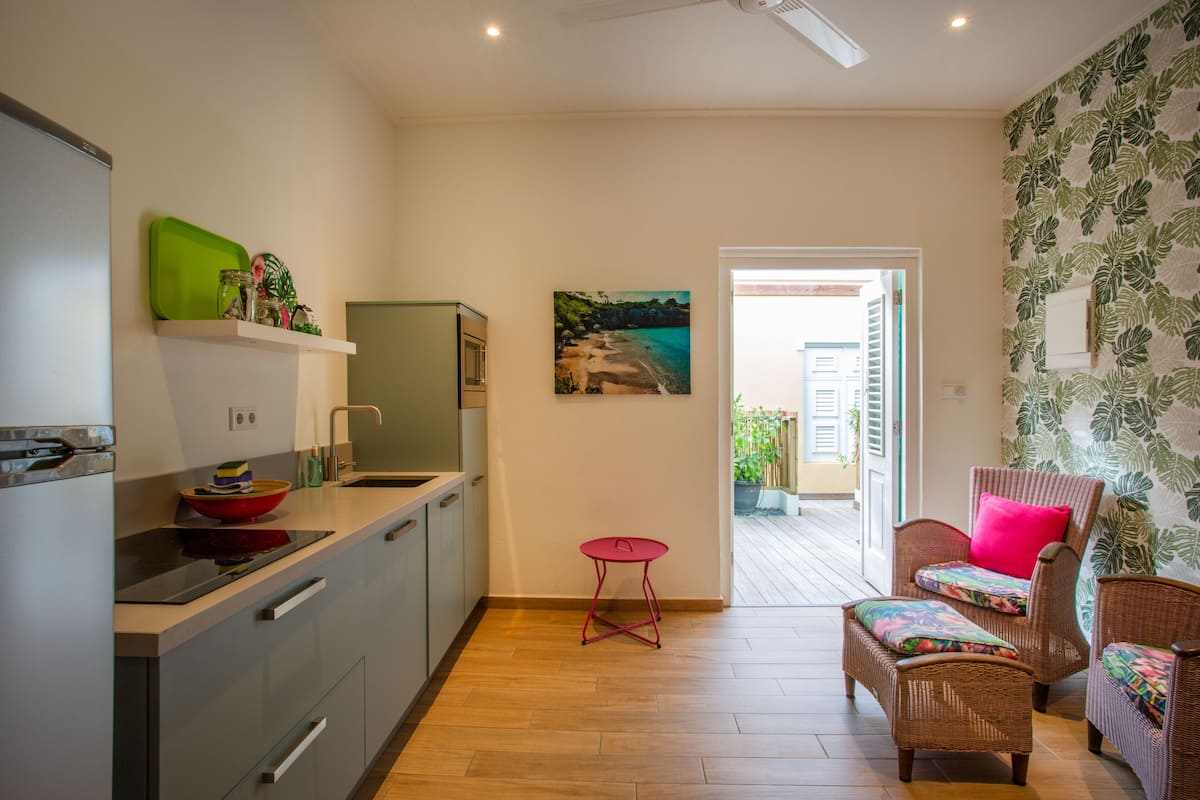 Una cocina moderna con un taburete rojo, mobiliario de mimbre y un cuadro de una playa.