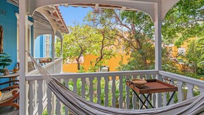 En balkon med hængekøje, træbakke og udsigt til træer og bygninger.