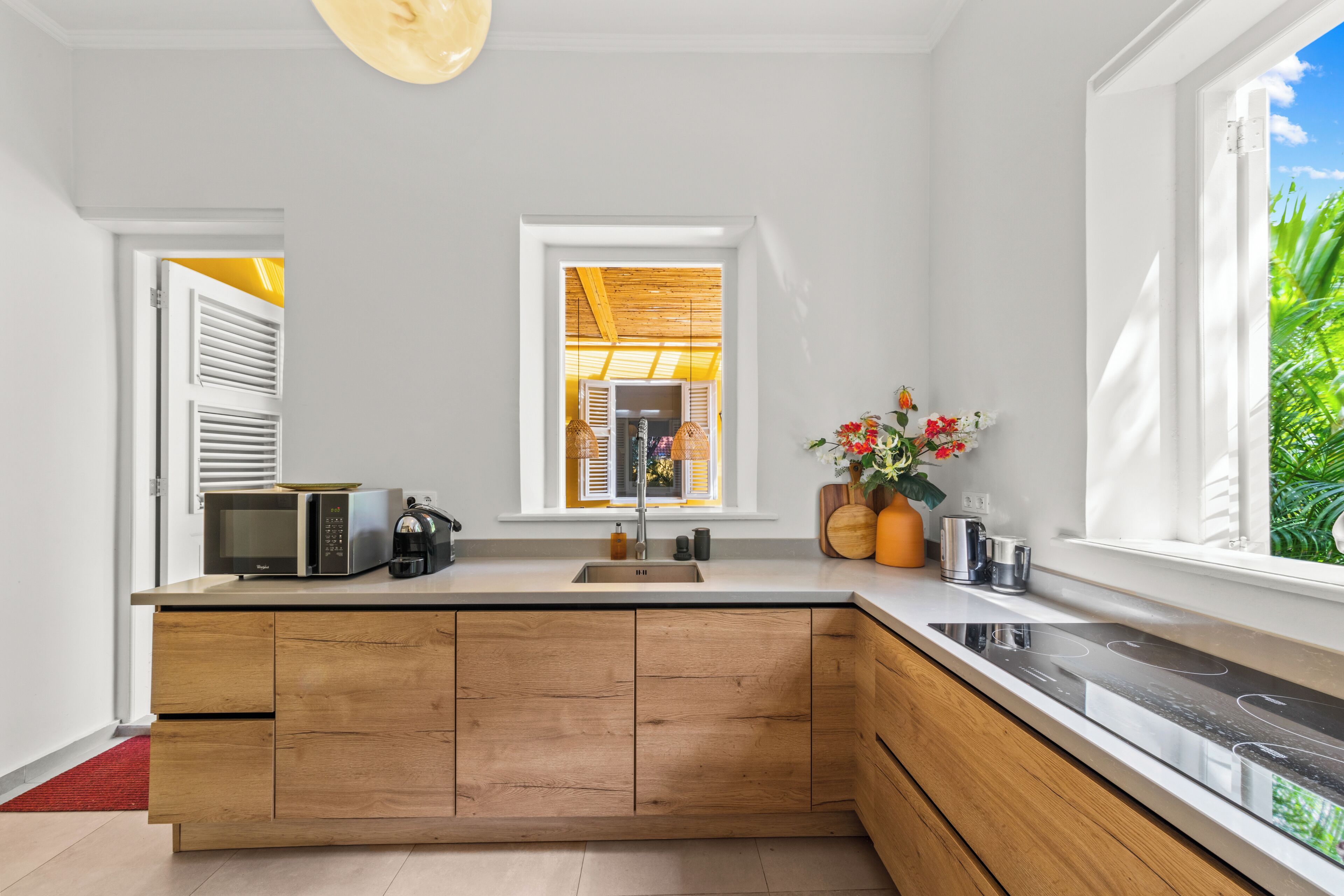 Una cocina moderna con una isla de madera, encimeras blancas, microondas integrado y ventana con vista a zonas verdes.