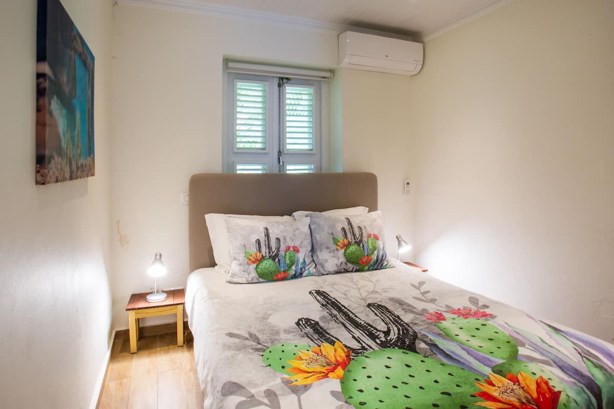 Un dormitorio con cama, una mesita de noche, una ventana con persianas y un aire acondicionado en la pared.