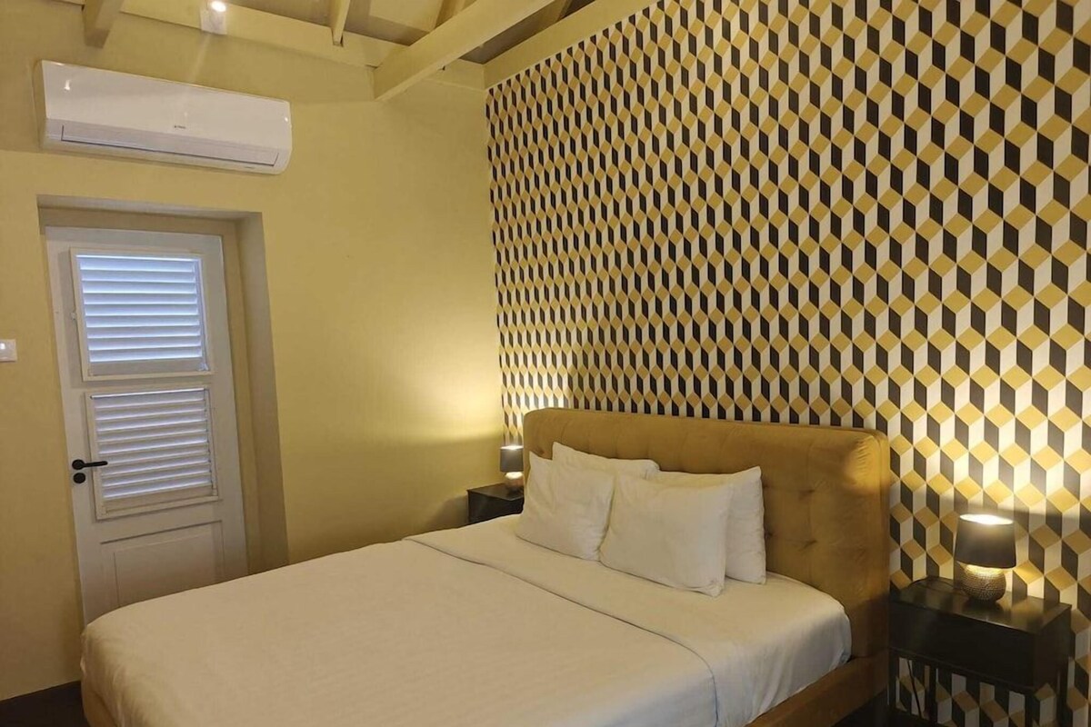 Une chambre d’hôtel avec un lit, un mur à motifs, une porte avec des stores et un appareil de climatisation.