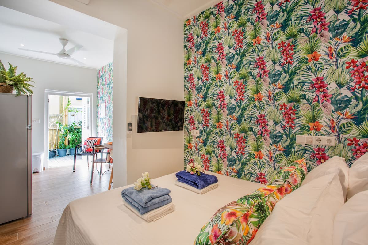 Un dormitorio con cama, una silla, una mesa con toallas y una pared con estampado floral.