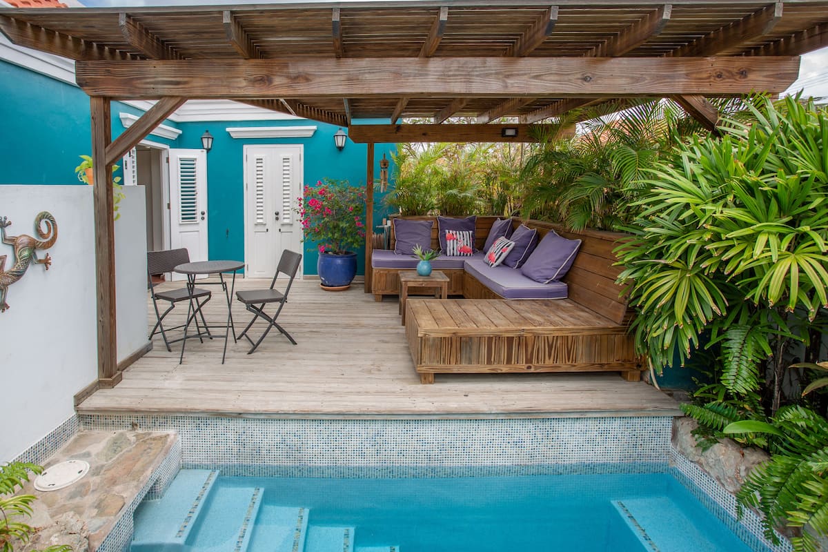 Terraza de madera con piscina, zona de estar y plantas en macetas.