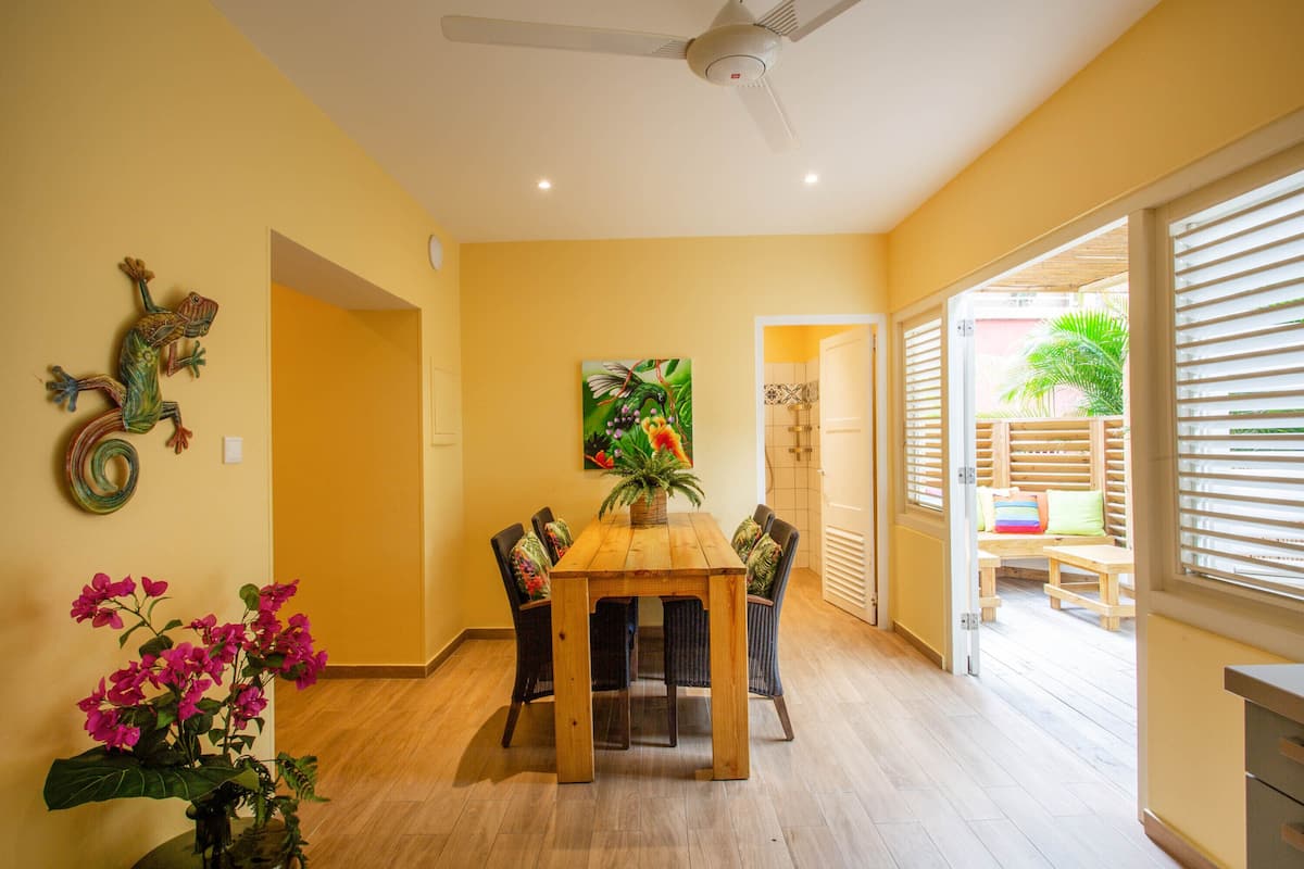 Comedor con mesa y sillas de madera, ventilador de techo y vista al exterior.