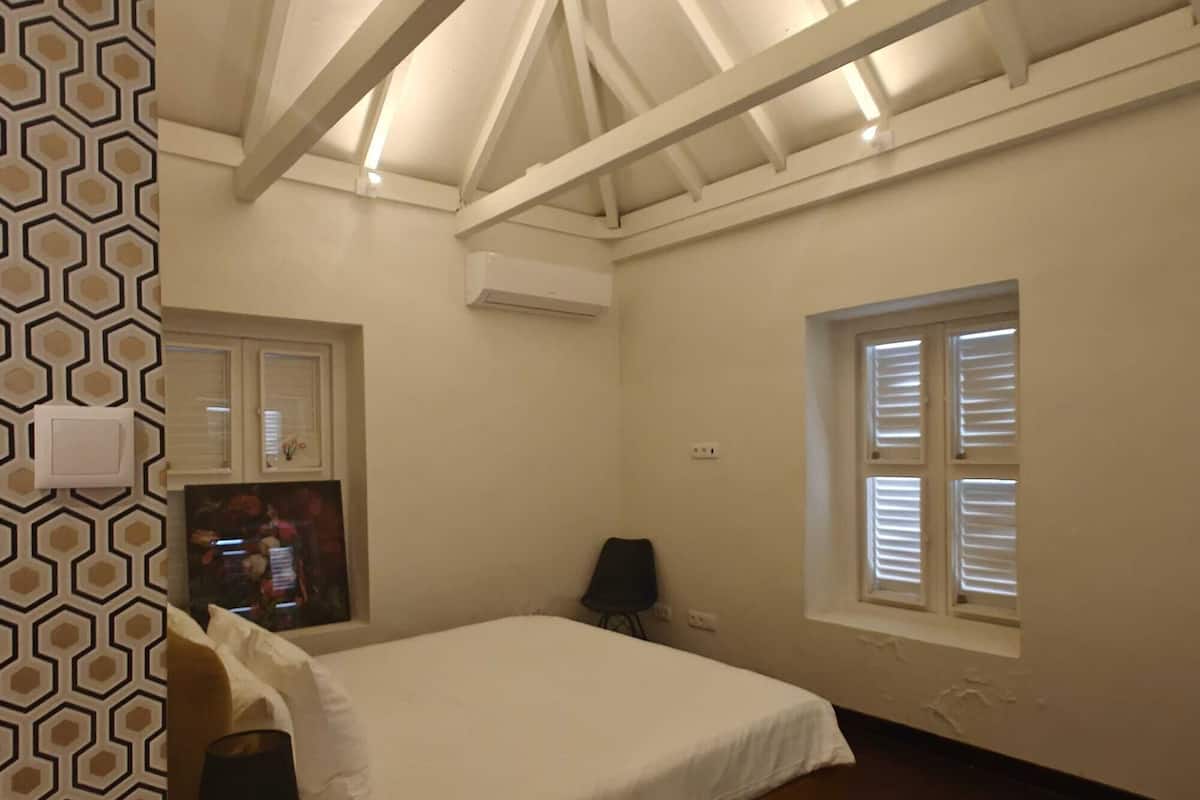 Un dormitorio con cama, ventana con persianas, aire acondicionado de pared y pared con diseño.