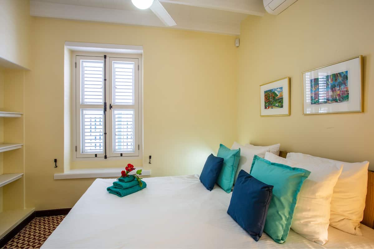 Habitación de hotel con una cama, almohadas, una ventana y dos cuadros en la pared.