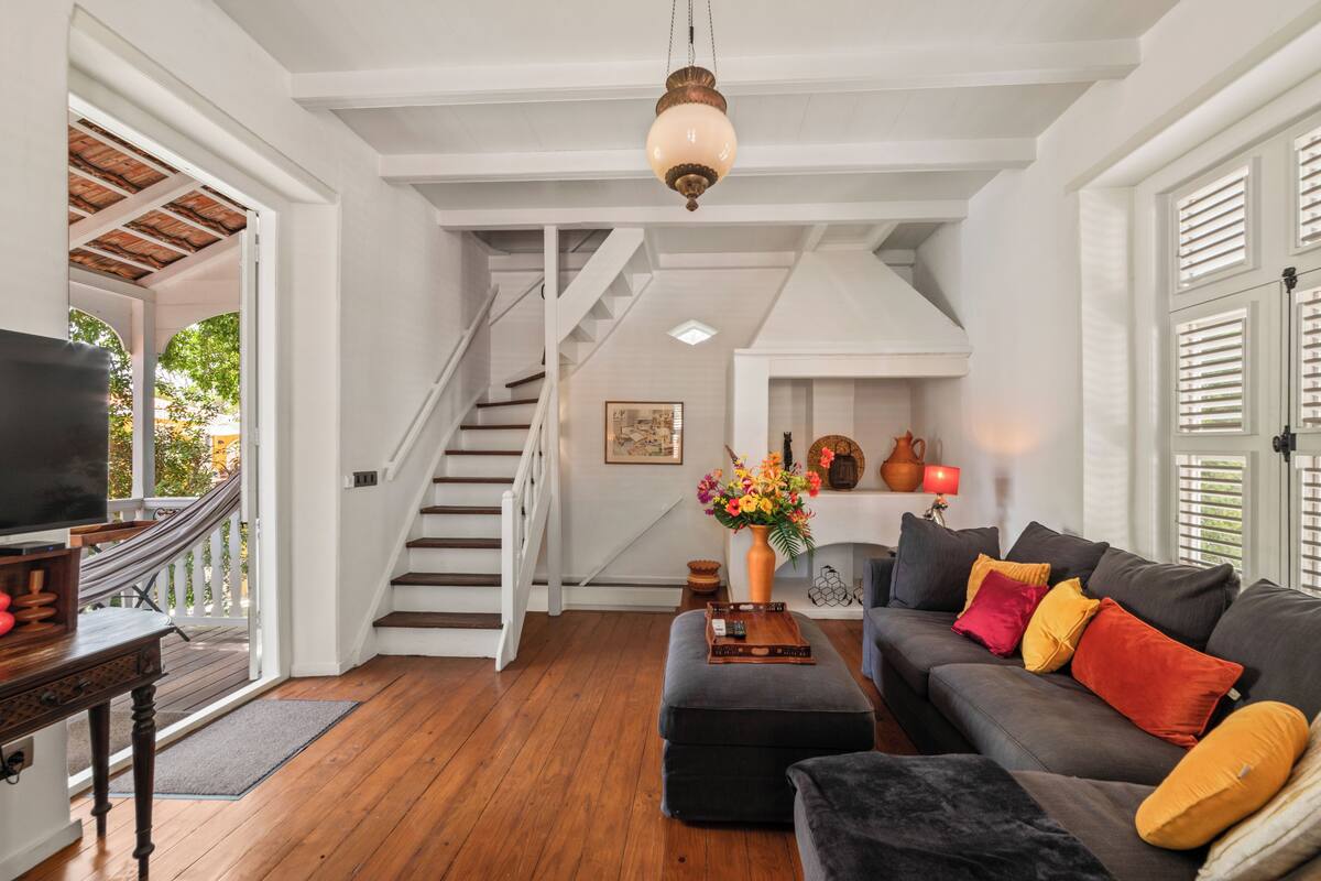 Un salón espacioso con escalera, un sofá con cojines coloridos, un televisor y una chimenea.