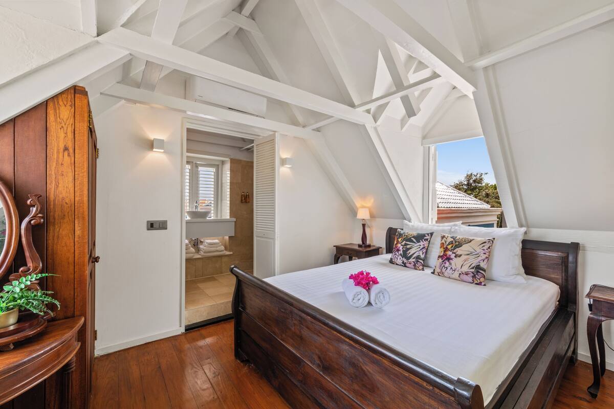 Un dormitorio con cama de madera, paredes blancas y techo inclinado.