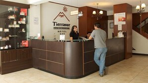 Un comptoir d’accueil d’hôtel avec une vitrine, une enseigne indiquant « TierraSur Hotel », et un escalier en arrière-plan.