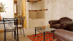 Un salon avec une table basse en verre, un canapé en cuir marron, un tapis à motifs et un coin repas comprenant une chaise et une table en métal.