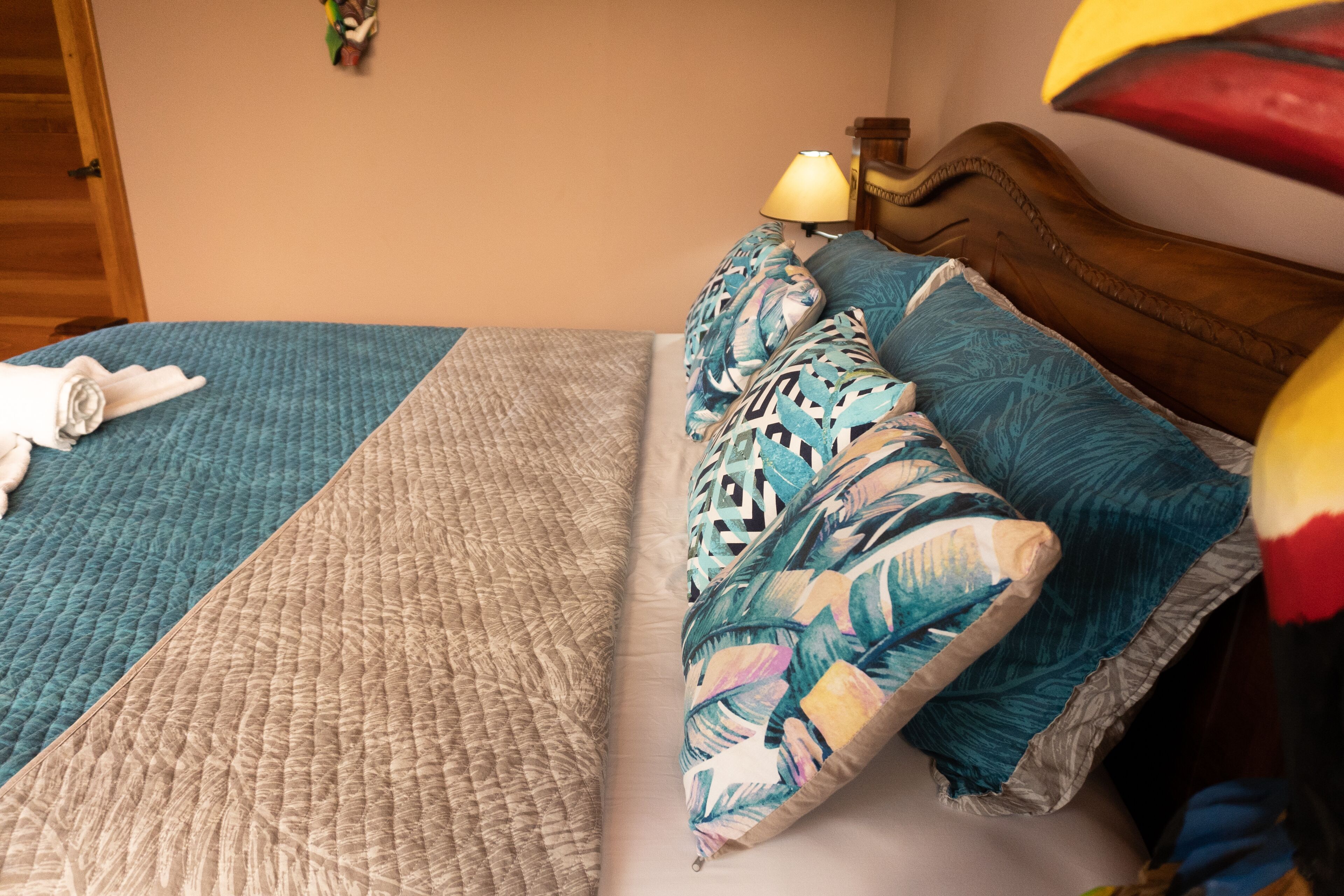 Una cama con un edredón azul, un edredón beige y varias almohadas con estampados de hojas tropicales.