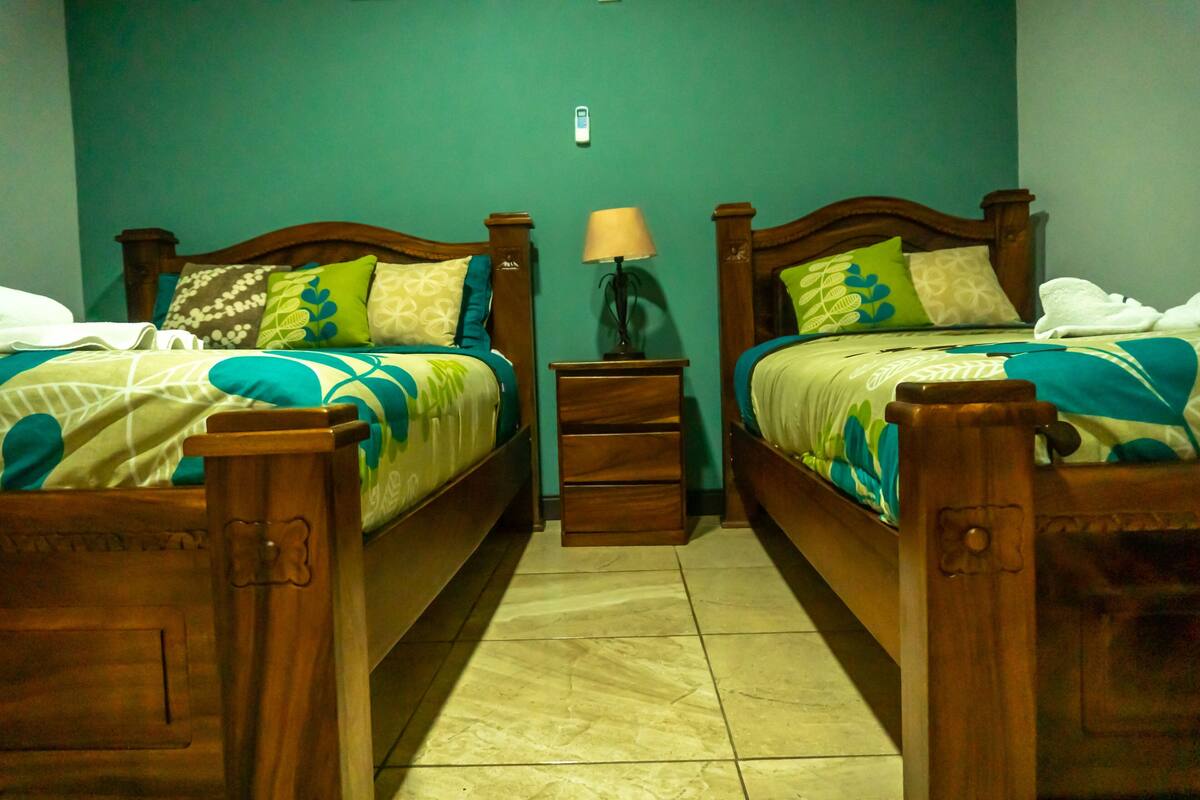 A twin room with two wooden beds, a nightstand with a lamp, and a small drawer unit.