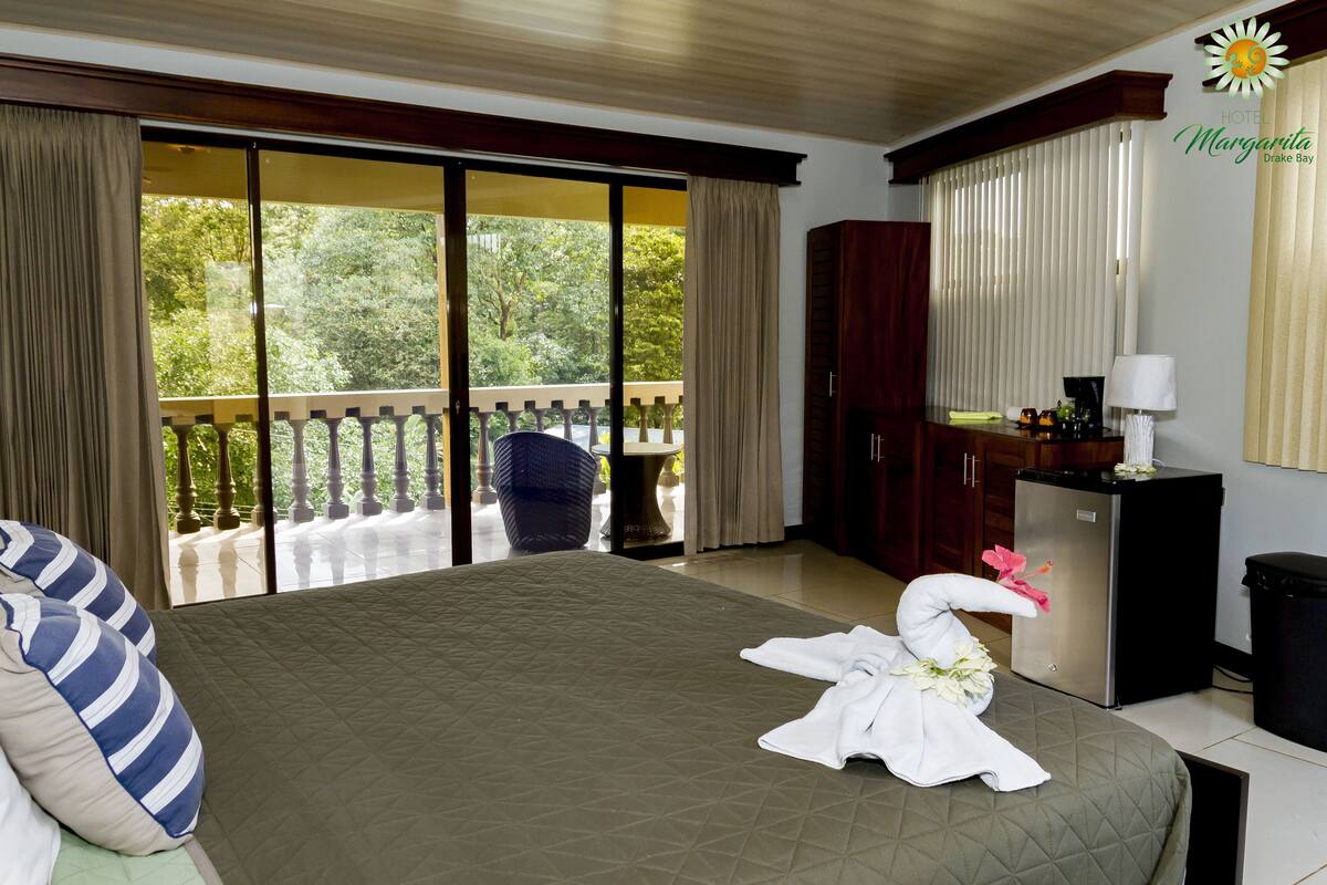 A hotel room with a large bed, a minibar, a desk with a lamp, and a view of the outdoors.
