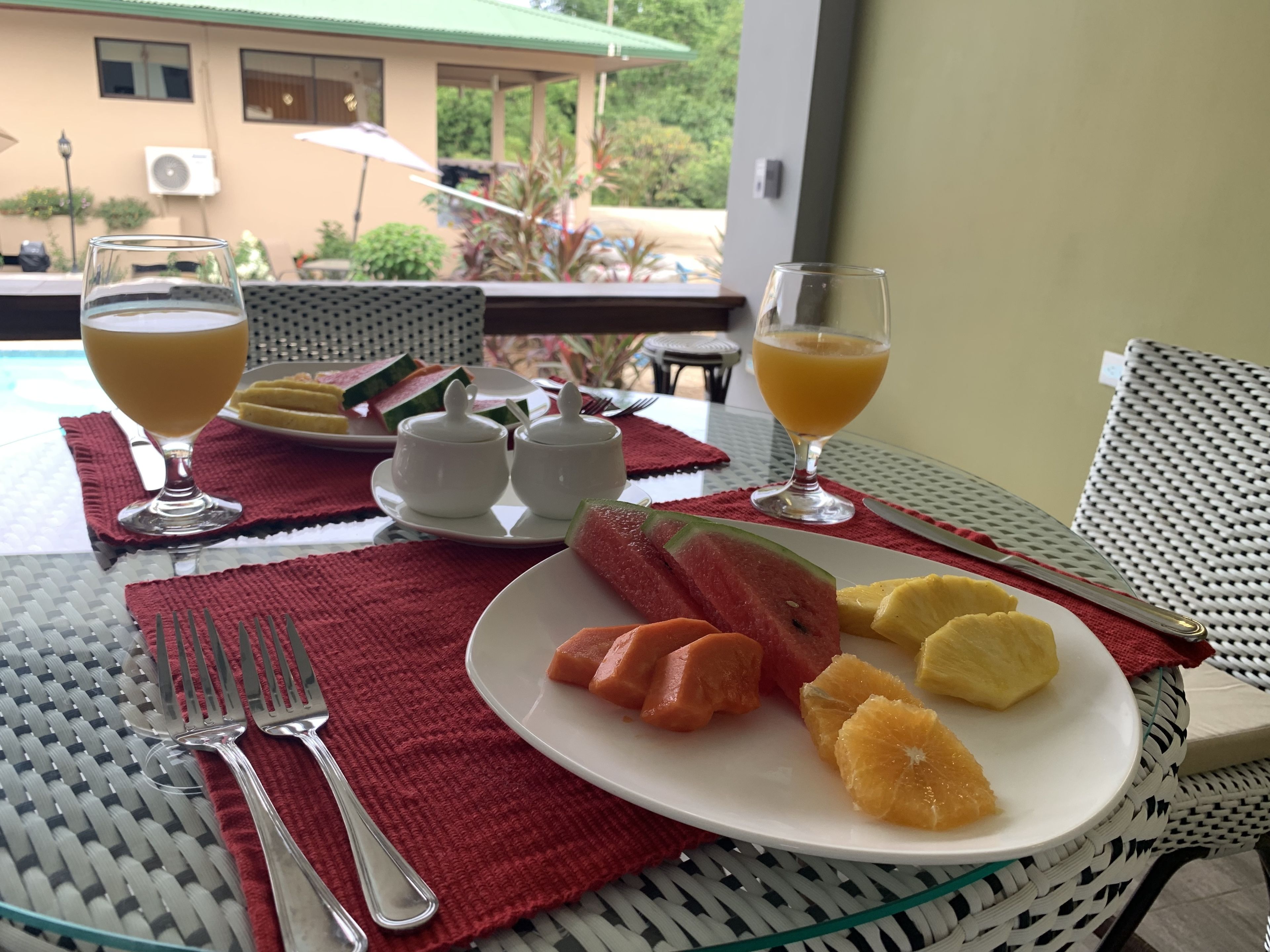 Ein Esstisch mit einer Fruchtschale, zwei Orangensaftgläsern und einer Wassermelone in Scheiben.