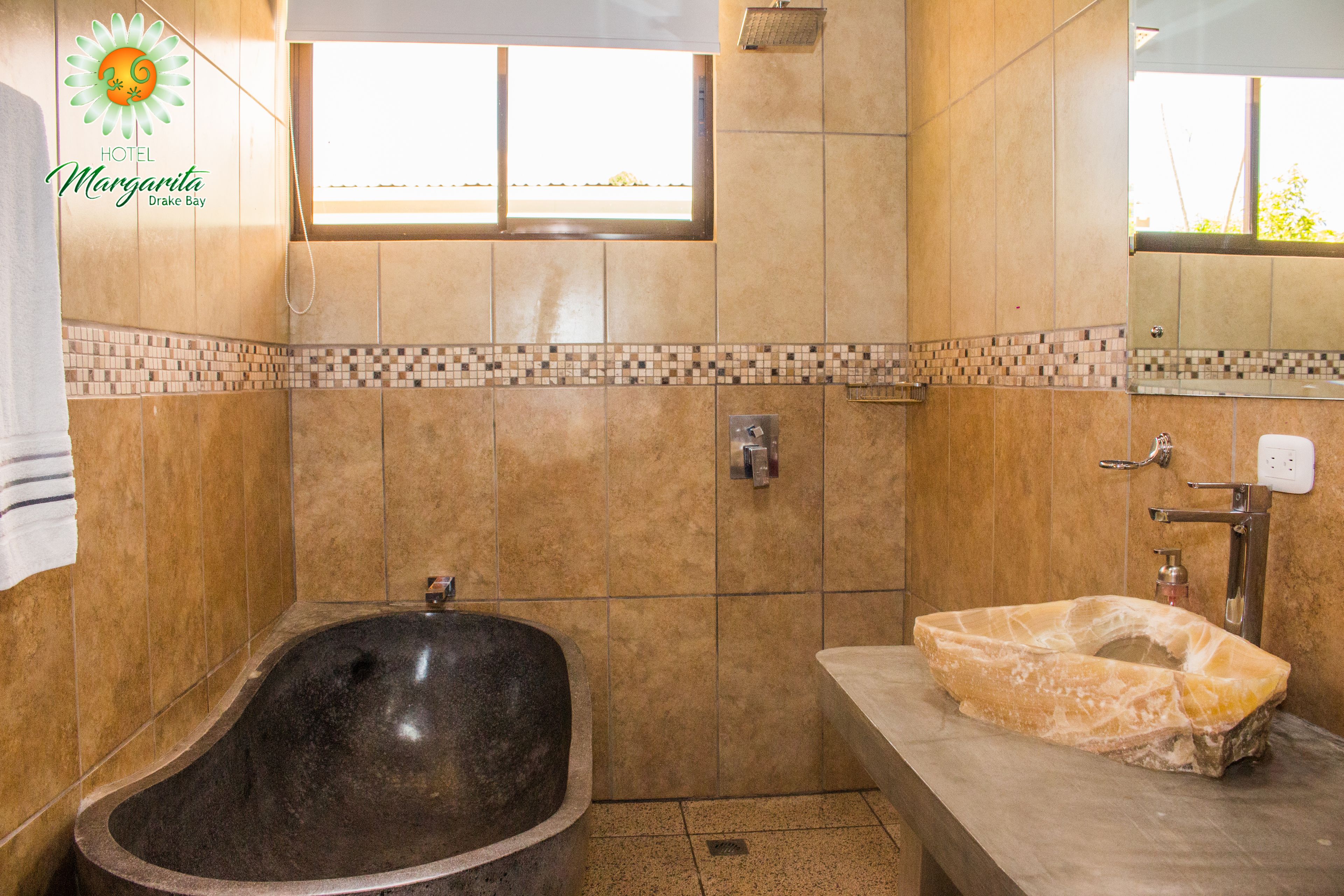 Un bagno con una vasca da bagno in pietra, un lavabo con piano in marmo e una zona doccia piastrellata.