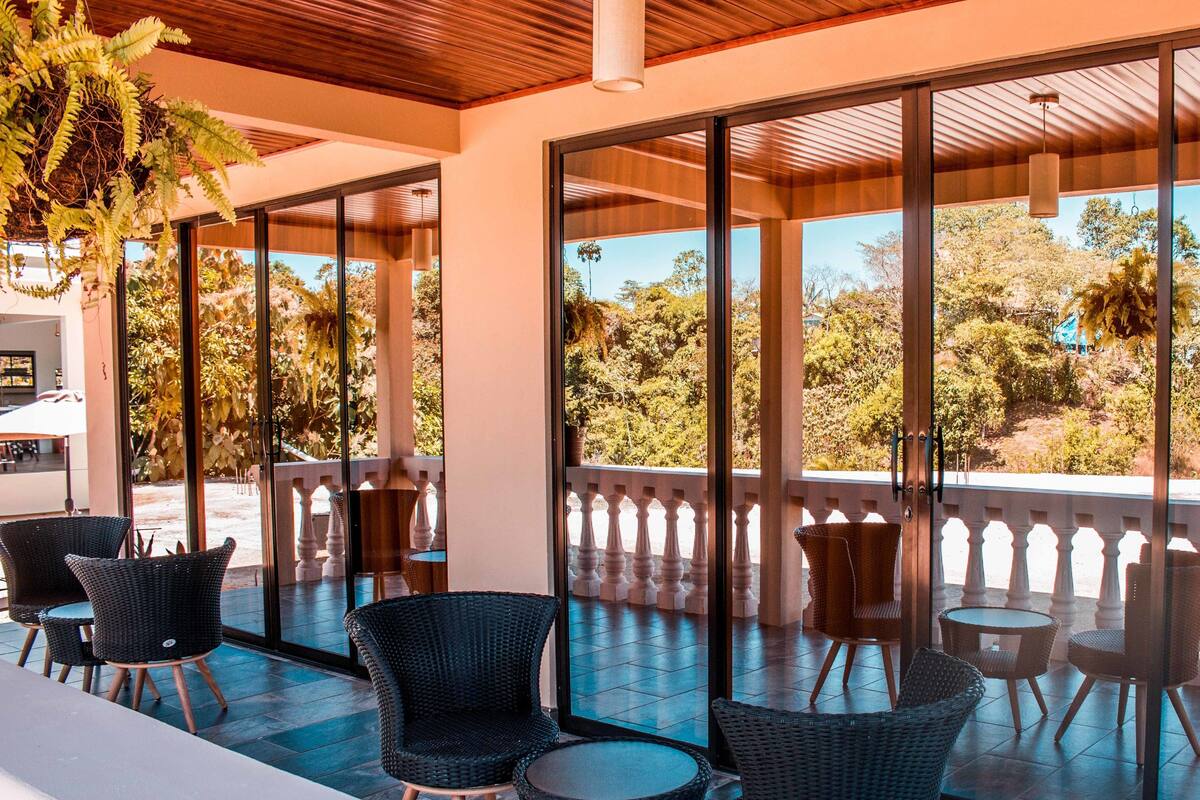 An outdoor seating area with wicker chairs and tables, large glass doors, and a view of trees and hills.