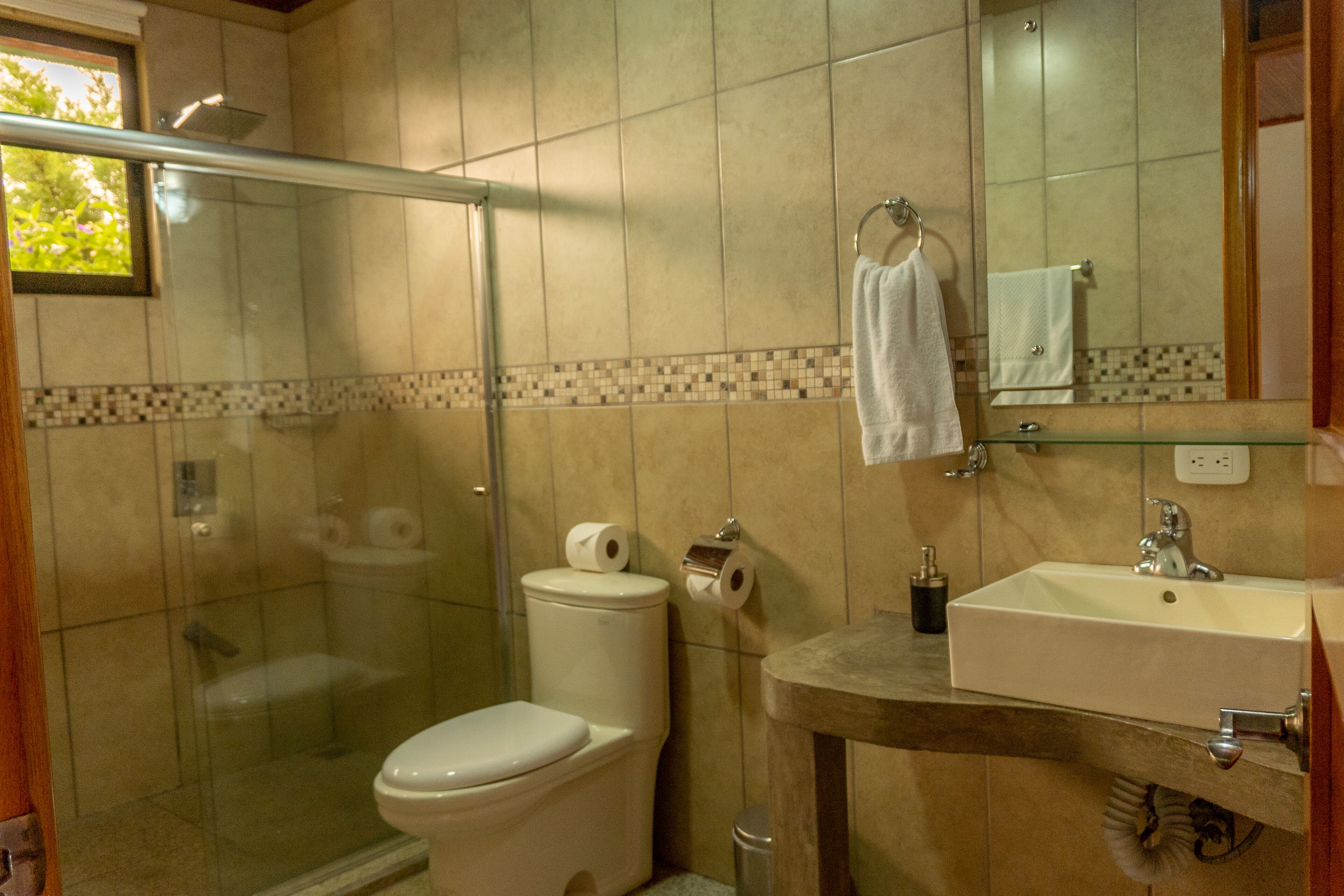 Un baño con cabina de ducha de vidrio, inodoro, lavamanos y espejo.