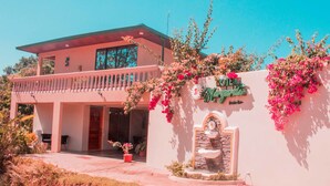 A two-story building with a balcony, a stone fountain, and a wall with a sign that reads "Hotel". - Hotel Margarita (Drake Bay)