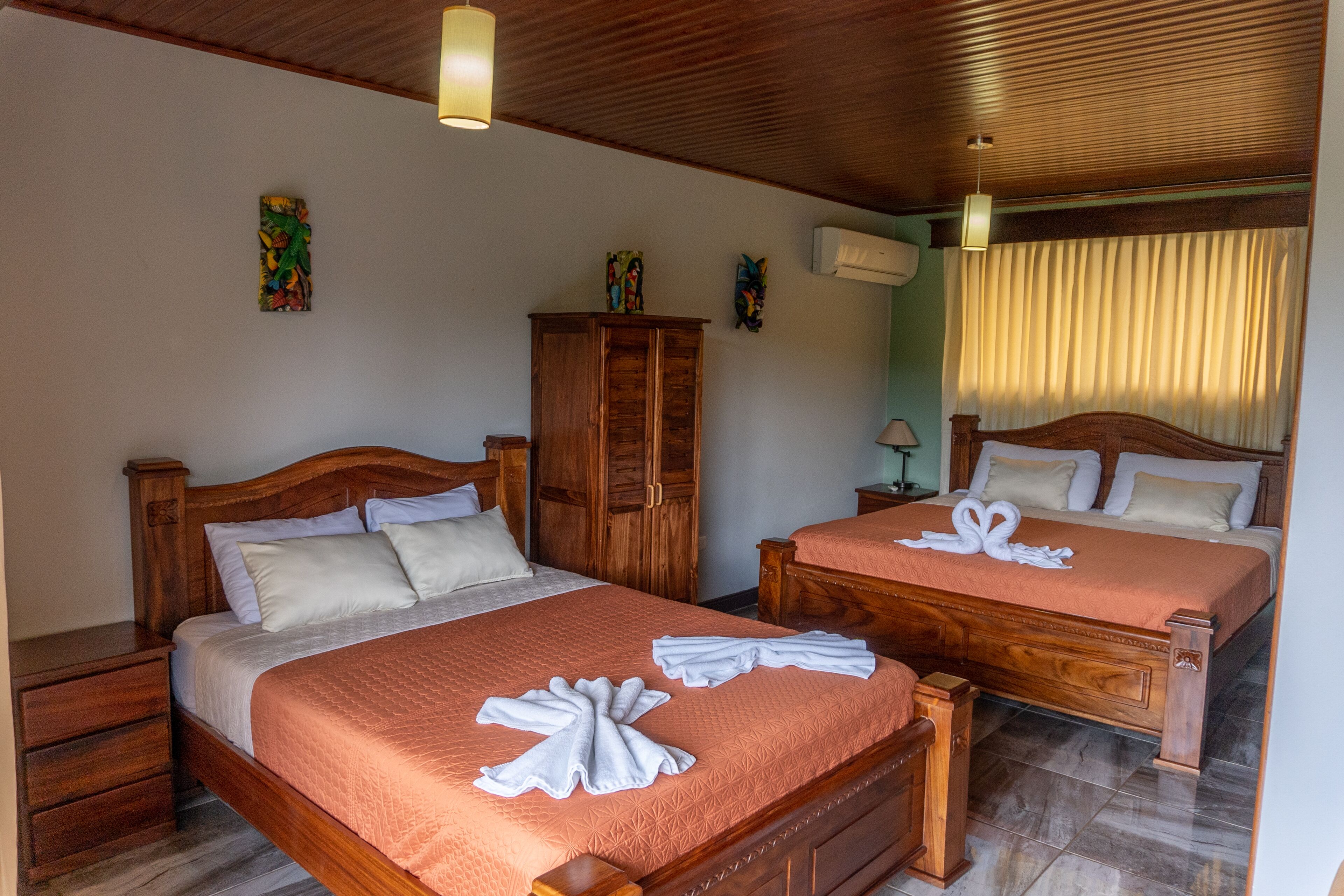 A hotel room with two wooden beds, each with a matching nightstand and a wooden wardrobe.