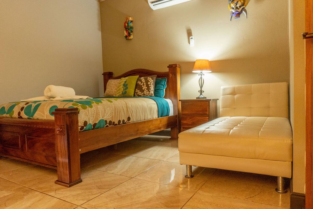 A bedroom with a wooden bed, a bedside table with a lamp, and a chair.