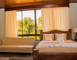 Una habitación de hotel con cama, sofá y un amplio ventanal con cortinas.