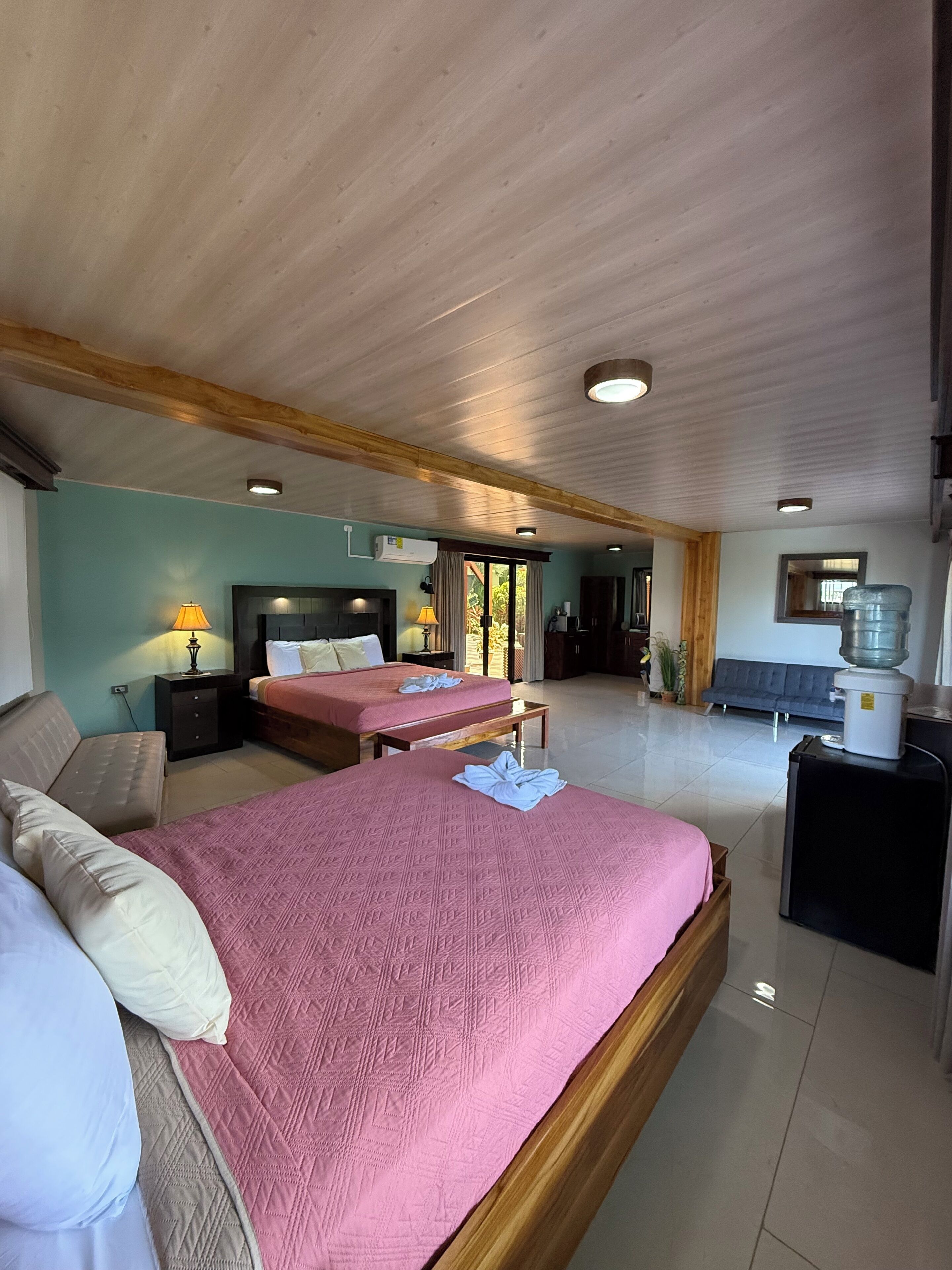 A spacious bedroom with two beds, a wooden ceiling, and a water dispenser.