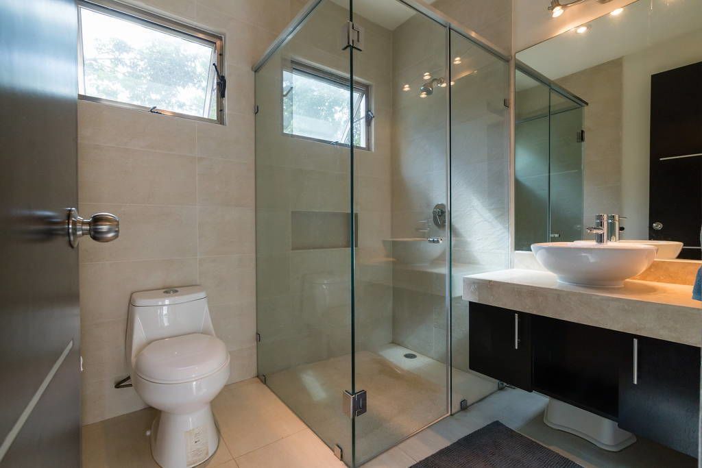 Un baño moderno con ducha de vidrio, inodoro blanco y un lavamanos grande con un espejo encima.