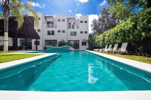 Una piscina con un edificio moderno al fondo, rodeada de vegetación.