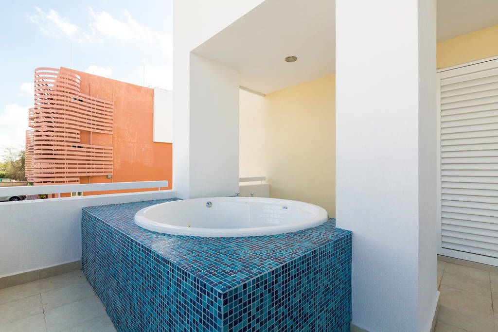 Ein modernes Whirlpool im Freien mit gefliestem Beckenrand, ein Balkon mit Blick auf ein hohes Gebäude und eine weiße Tür.