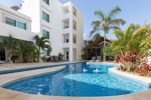 A swimming pool surrounded by palm trees and a white building with balconies. - Awah by CocoBR (Playa del Carmen)