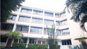 Un hotel de varios pisos con un patio central, que cuenta con una piscina, palmeras y un área de descanso con sombrillas.