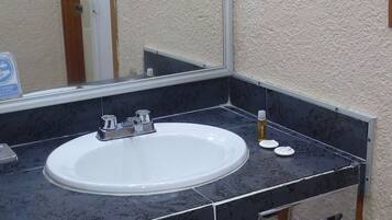 A bathroom with a white sink, black countertop, and a mirror. There is a towel rack above the sink and a door in the background.