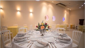 Una mesa de comedor redonda con mantel blanco, platos, cubiertos y un centro de mesa con flores.