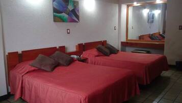 A hotel room with two beds, each with a red bedspread and brown pillows. There is a mirror on the wall and a painting above the beds.