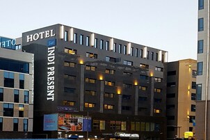 Un moderno edificio de hotel con un llamativo letrero que dice "HOTEL INDIPRESENT", varios pisos y ventanas iluminadas.