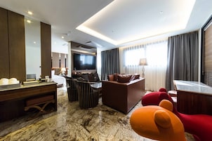 Habitación de hotel moderna con una gran televisión de pantalla plana, un sofá, un comedor y suelo de mármol.