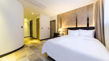 A hotel room with a large bed, a nightstand with a lamp, a wall-mounted TV, and a curved wall design.