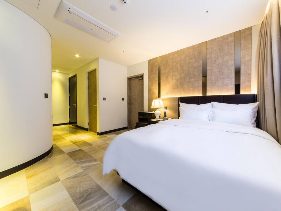 A hotel room with a large bed, a nightstand with a lamp, a wall-mounted TV, and a curved wall design.