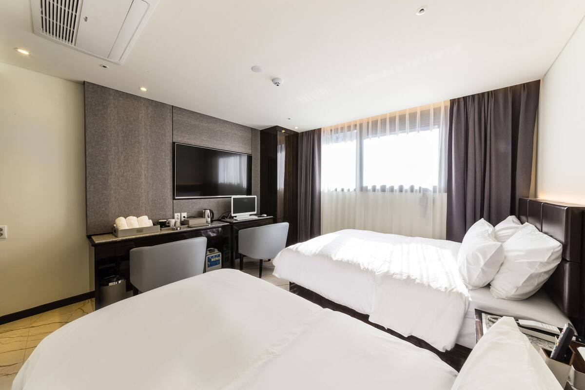 Una habitación de hotel con una cama, un escritorio con computadora, televisor y ventana con cortinas.