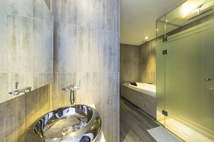 Un baño moderno con un lavabo grande y reflectante, una cabina de ducha con mampara de vidrio y un revestimiento de pared de mármol.
