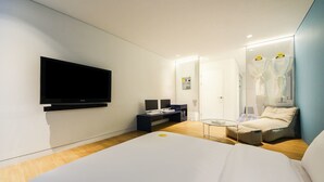 Una habitación de hotel moderna con una cama grande, un escritorio con computadora, un televisor de pantalla plana y un área de descanso con una silla y una mesita.