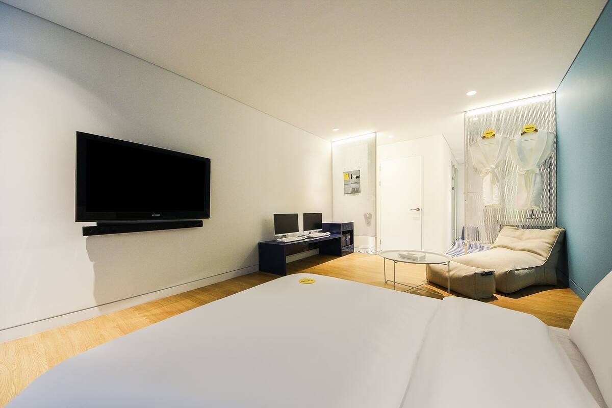 Ein modernes Hotelzimmer mit einem großen Bett, einem Schreibtisch mit Computer, einem Flachbildfernseher und einer Sitzecke mit Stuhl und kleinem Tisch.