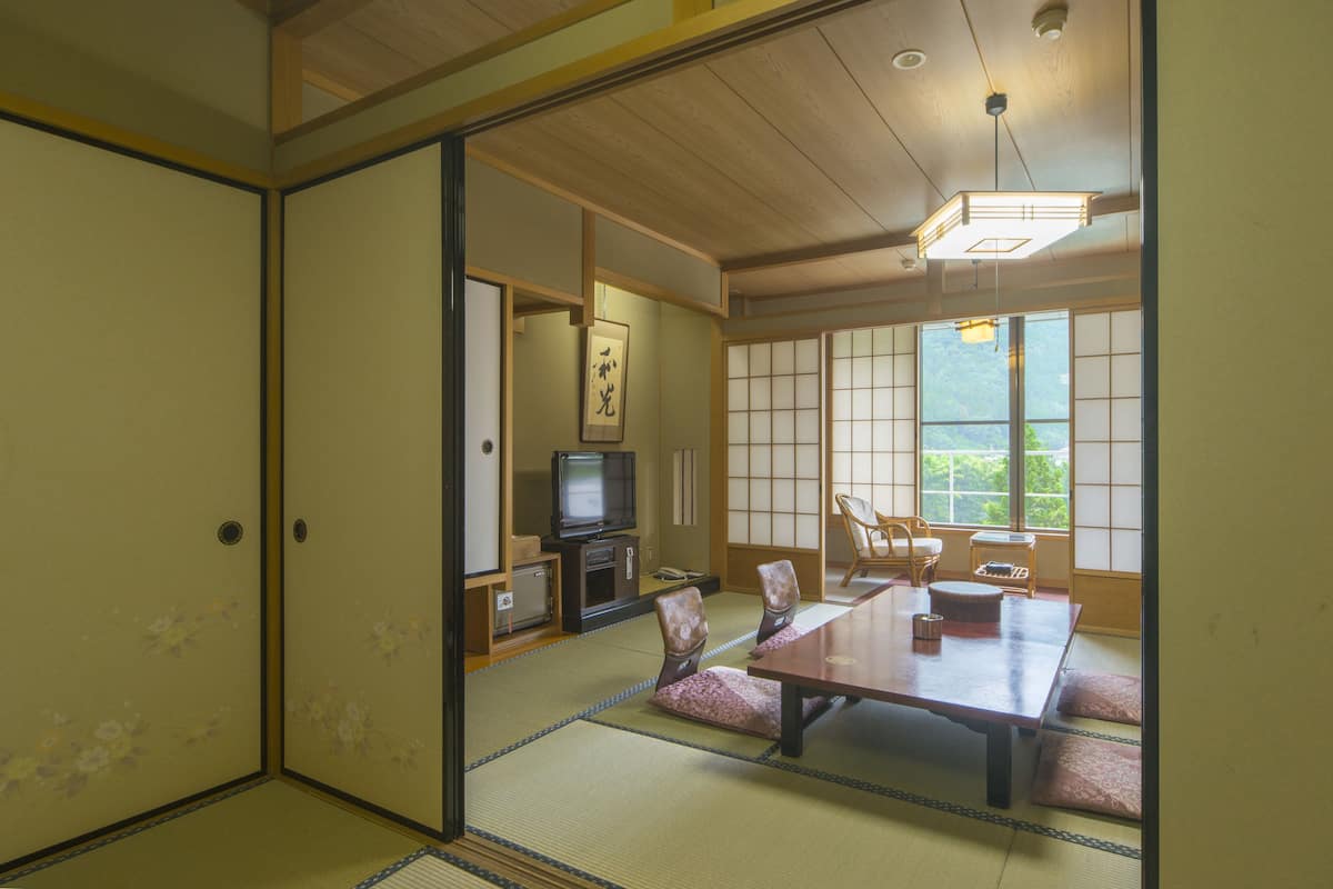 A traditional Japanese room with tatami flooring, a low table with cushions, a television, and sliding doors.