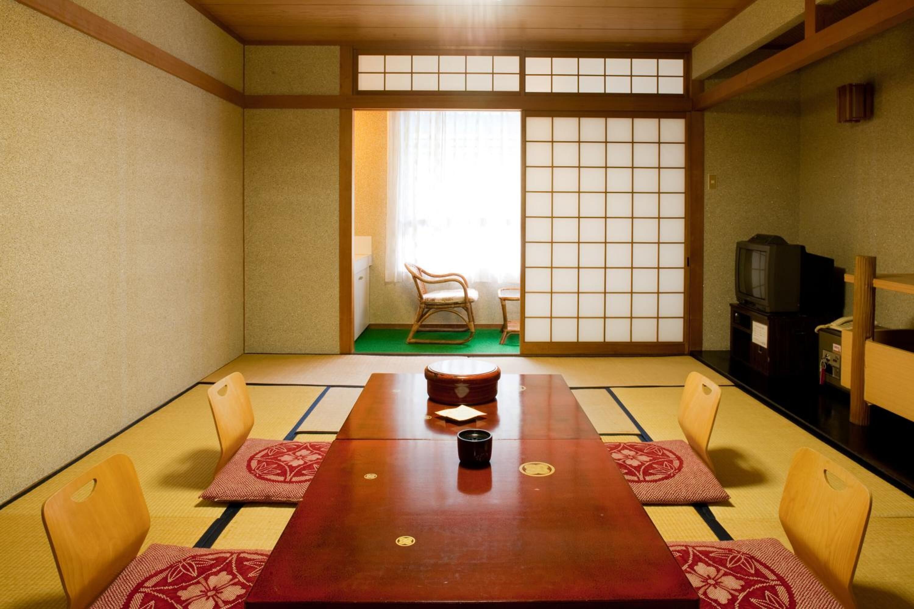 A traditional Japanese room with tatami flooring, a low table with cushions, and a sliding door with a view to the outside.