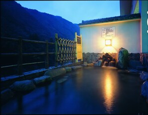 A traditional Japanese onsen with a wooden fence, a stone wall, and a lit signboard. - Hotel Gujo Hachiman (Gujo)