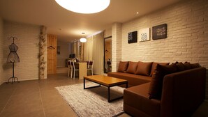 A modern living room with a brown sofa, a wooden coffee table, and a white brick wall. - May AVE (Yeoju)